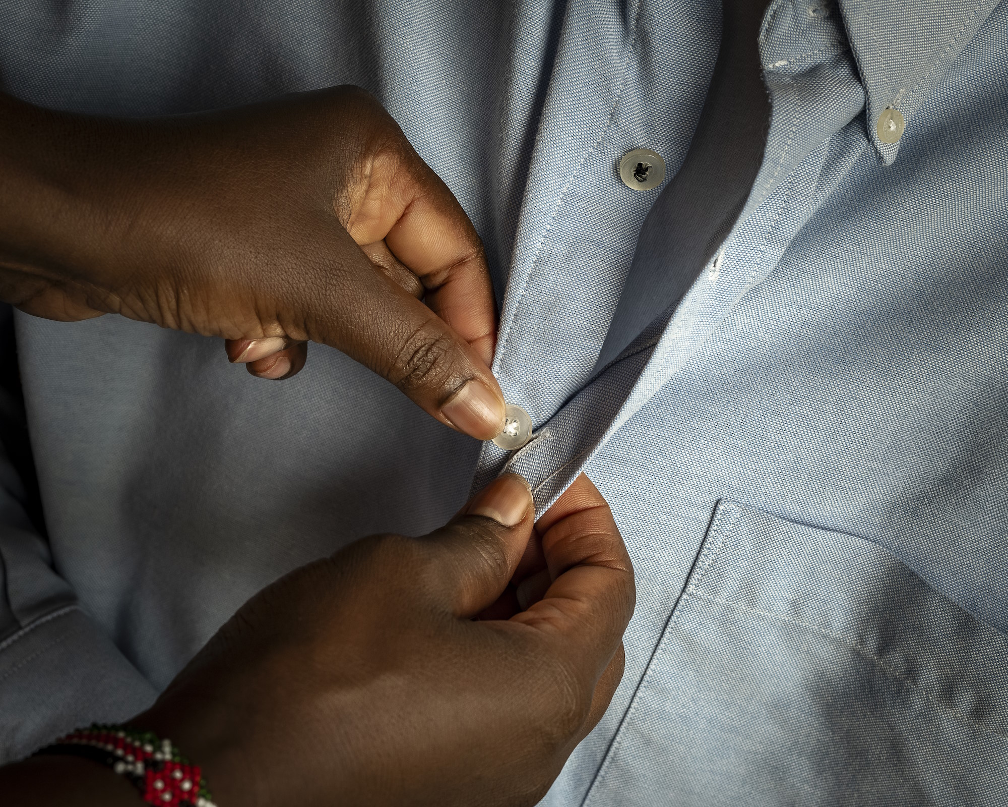 Mani di una persona che abbottona camicia